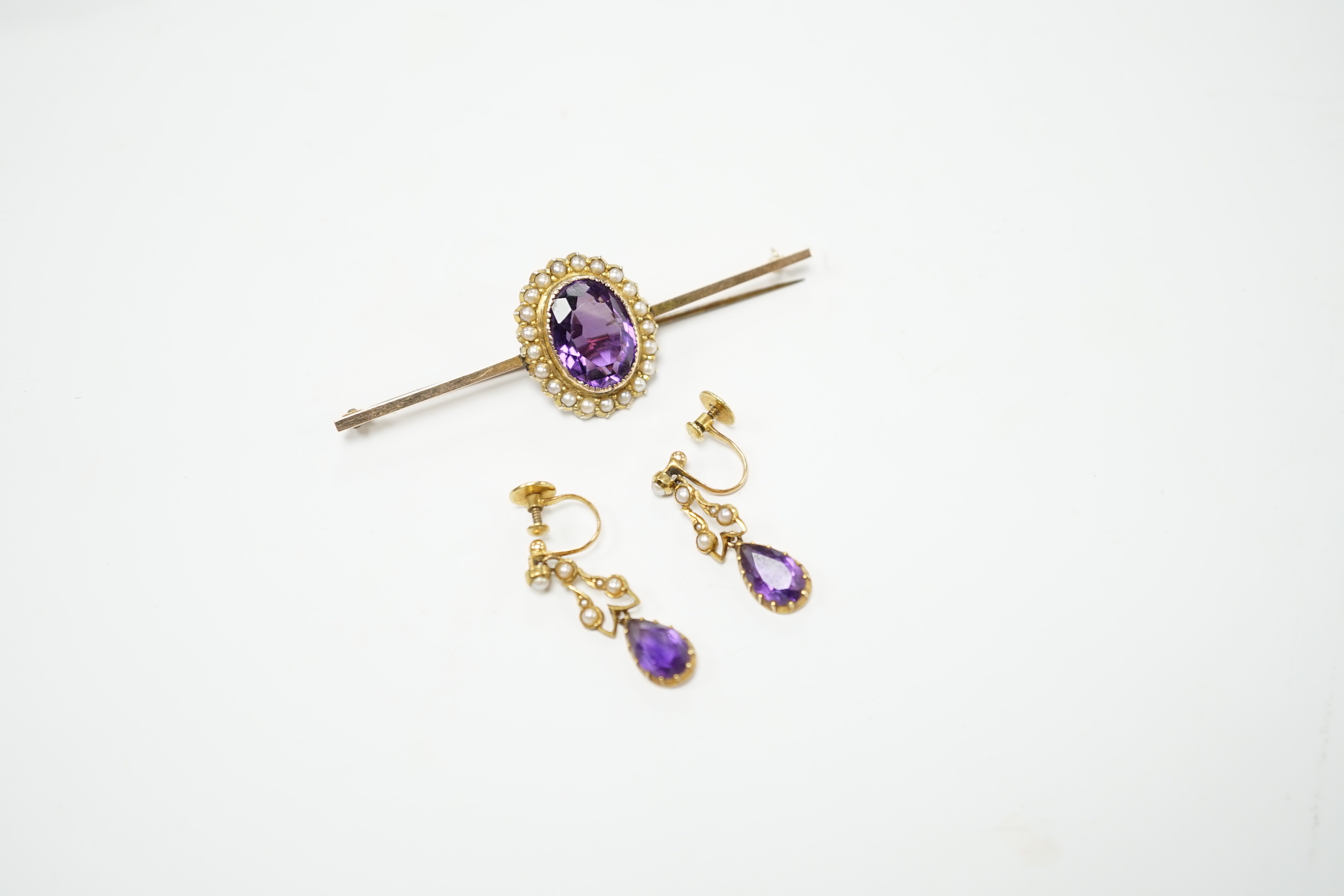 A yellow metal, amethyst and seed pearl cluster set bar brooch, 65mm and a pair of similar drop ear clips, gross weight 10 grams.